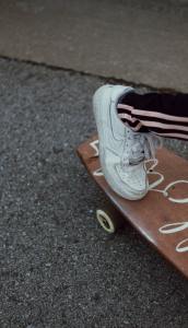 Photo of a foot wearing a white shoe pushing off of a wooden longboard